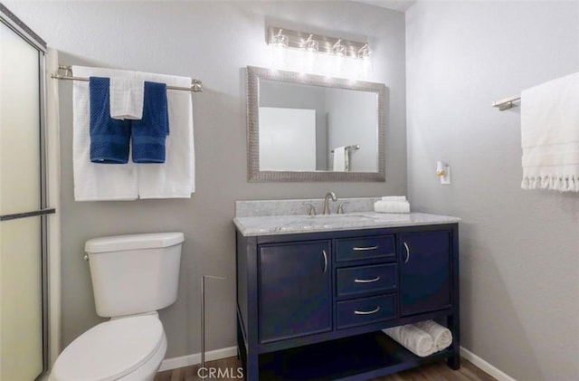 full bathroom featuring toilet, vanity, baseboards, wood finished floors, and a shower with door