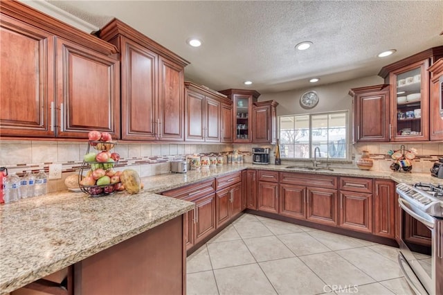 kitchen with a sink, stainless steel stove, decorative backsplash, light tile patterned floors, and light stone countertops