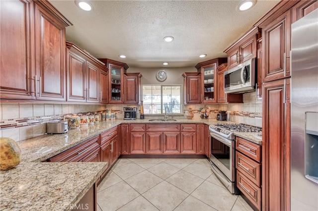 kitchen with appliances with stainless steel finishes, a sink, a textured ceiling, light stone countertops, and backsplash