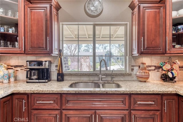 kitchen featuring a sink, glass insert cabinets, tasteful backsplash, and light stone counters