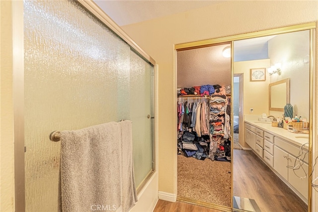 full bathroom featuring wood finished floors, double vanity, and combined bath / shower with glass door