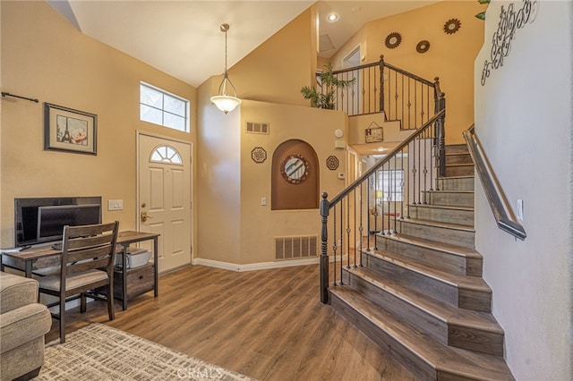 entrance foyer with wood finished floors, high vaulted ceiling, stairs, baseboards, and arched walkways