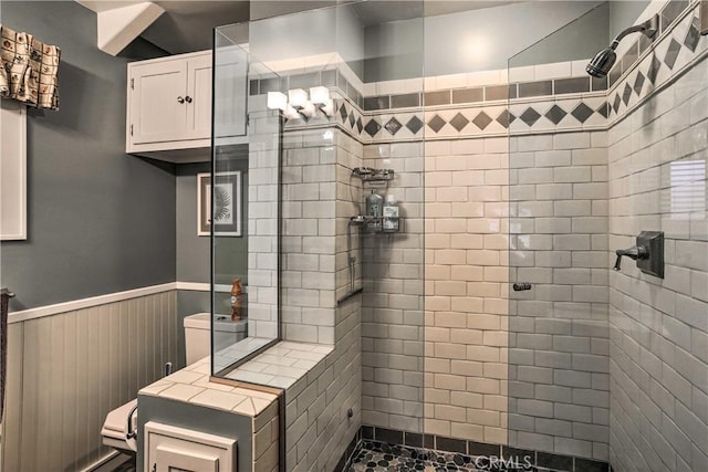 full bathroom featuring a wainscoted wall, tiled shower, and toilet