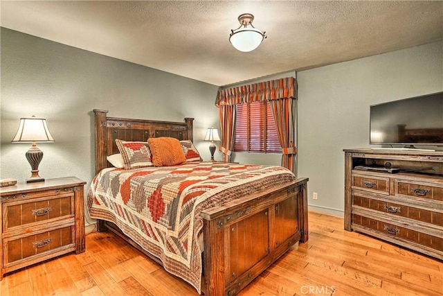 bedroom with light wood-style floors, baseboards, and a textured ceiling