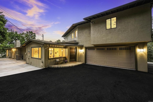 view of property with asphalt driveway, stucco siding, a chimney, and central AC
