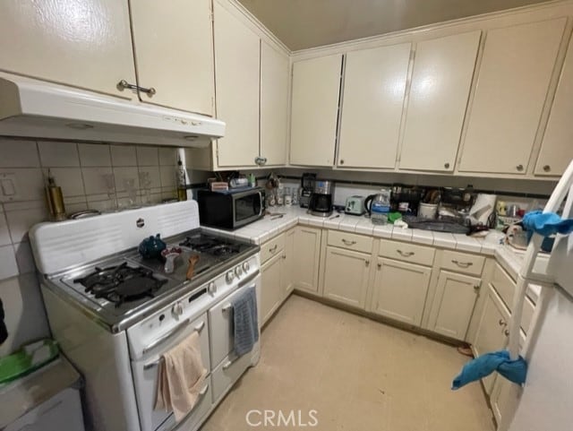 6705 Denny Ave, North Hollywood, CA 91606 - kitchen featuring range with two ovens, stainless steel microwave, under cabinet range hood, tile counters, and decorative backsplash
