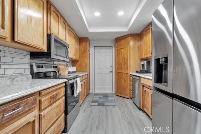 25624 Castlerock Rd, Apple Valley, CA 92308 - kitchen featuring stainless steel appliances, a raised ceiling, light wood-style flooring, decorative backsplash, and light countertops