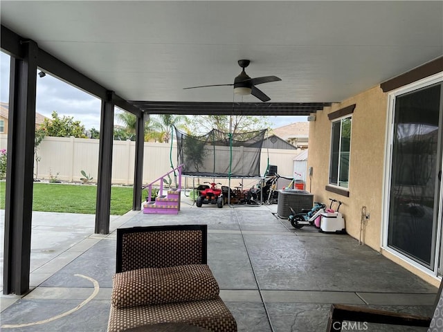 view of patio featuring a trampoline, fence, central air condition unit, and a ceiling fan