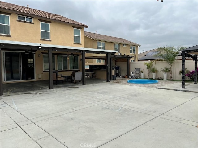 rear view of house with fence, a patio, stucco siding, a gazebo, and a tiled roof
