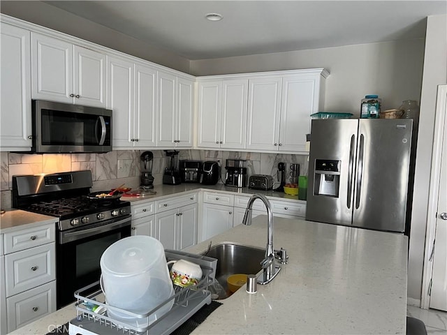 kitchen with stainless steel appliances, a sink, white cabinetry, tasteful backsplash, and light stone counters