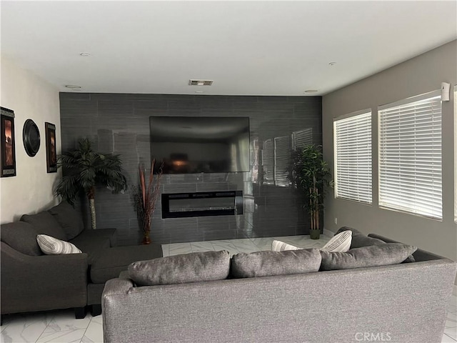 living area featuring marble finish flooring, a glass covered fireplace, and an accent wall