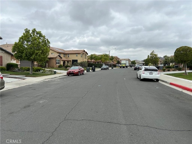 view of asphalt street with a residential view, sidewalks, curbs, and street lights