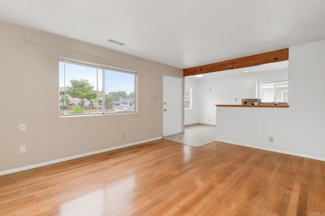 unfurnished living room featuring light wood-type flooring, baseboards, and beamed ceiling