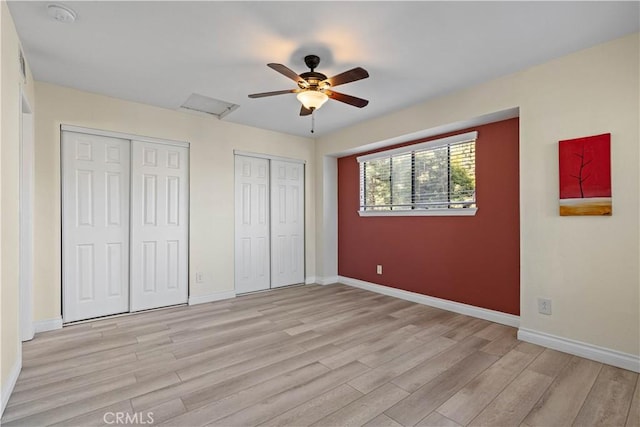 unfurnished bedroom with two closets, light wood finished floors, baseboards, and ceiling fan