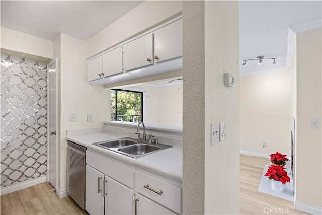 kitchen featuring dishwasher, a sink, light wood-style floors, white cabinets, and light countertops