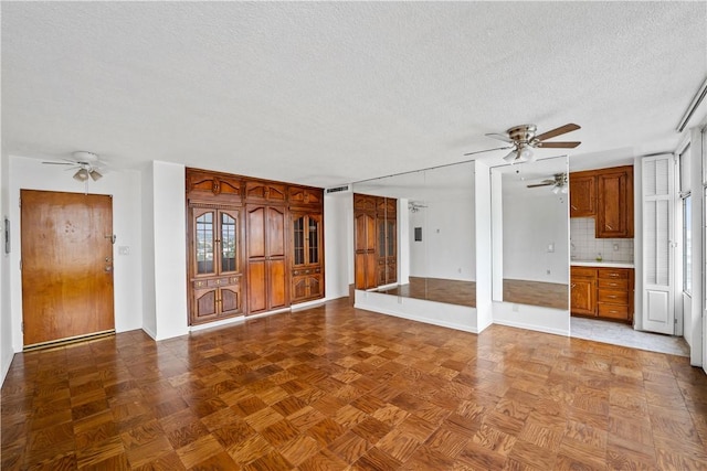 unfurnished living room featuring a ceiling fan, a textured ceiling, and baseboards