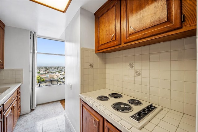 kitchen featuring white electric stovetop, decorative backsplash, tile counters, brown cabinetry, and light tile patterned floors