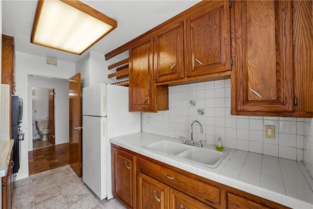 kitchen featuring a sink, freestanding refrigerator, brown cabinets, tasteful backsplash, and tile countertops