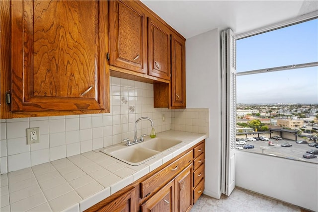 kitchen with a sink, decorative backsplash, brown cabinetry, and tile countertops