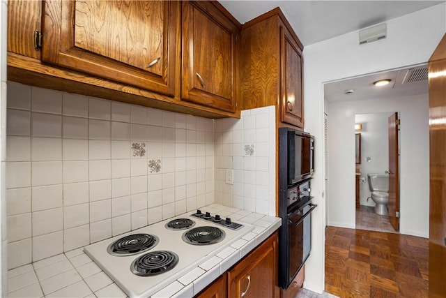 kitchen featuring tile countertops, black appliances, tasteful backsplash, brown cabinetry, and baseboards