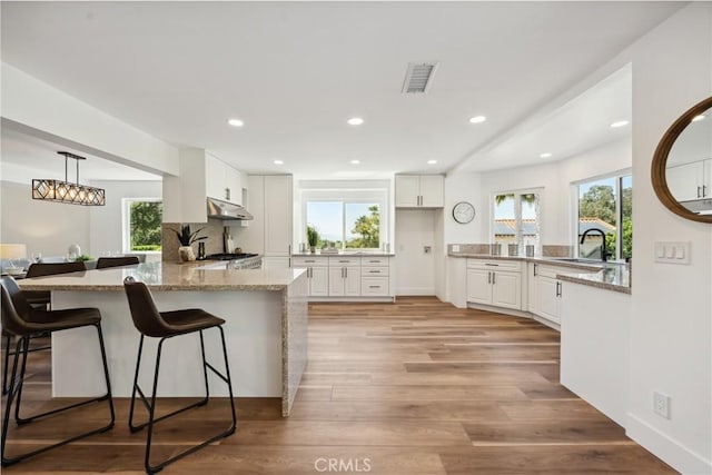 529 Manzanita Rd, Redlands, CA 92373 - kitchen with under cabinet range hood, a sink, white cabinetry, a kitchen breakfast bar, and recessed lighting