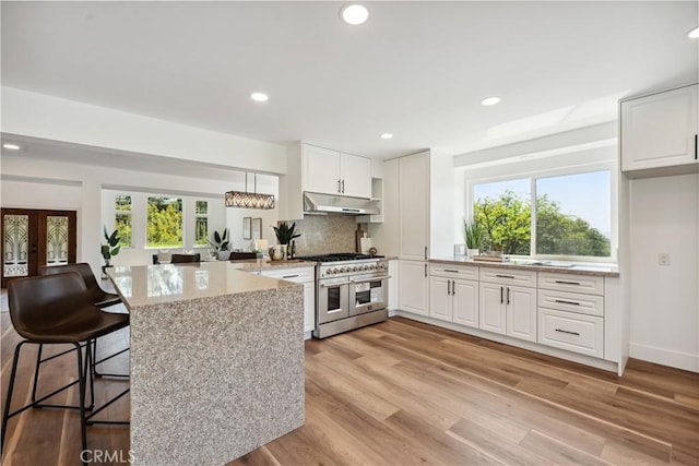 529 Manzanita Rd, Redlands, CA 92373 - kitchen featuring double oven range, under cabinet range hood, white cabinetry, light stone countertops, and a peninsula