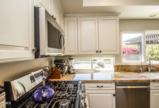 kitchen featuring stainless steel appliances, a sink, white cabinetry, and light stone counters