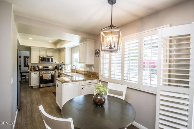 kitchen with appliances with stainless steel finishes, dark wood-style floors, a chandelier, decorative light fixtures, and a peninsula