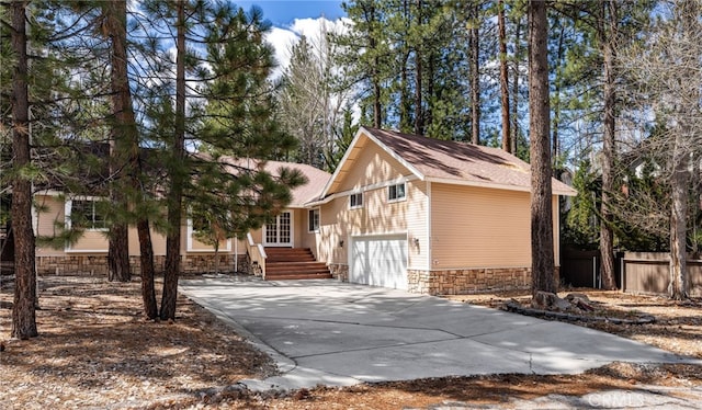 view of front of house featuring stone siding, fence, concrete driveway, a garage, and roof with shingles