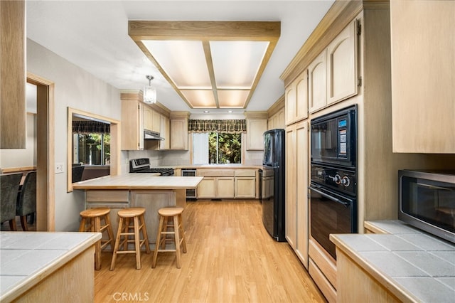 kitchen with black appliances, light brown cabinetry, light wood-style floors, a peninsula, and under cabinet range hood