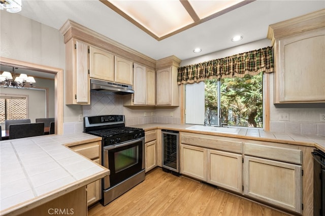 kitchen with gas stove, beverage cooler, under cabinet range hood, light brown cabinets, and recessed lighting