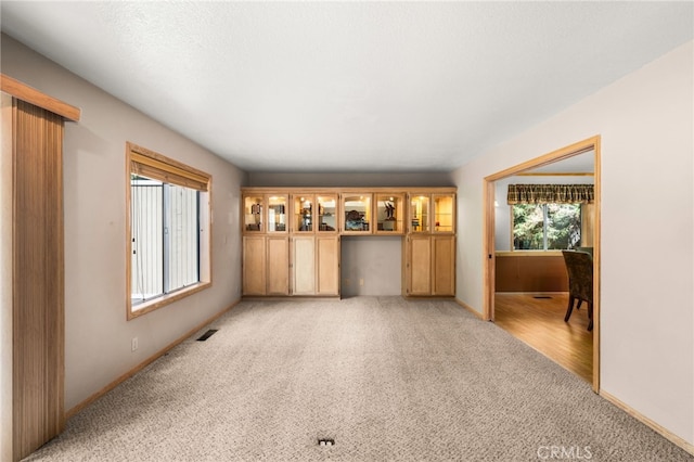 unfurnished living room featuring light colored carpet and baseboards