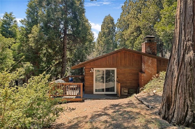 rear view of property with a chimney, a deck, and a forest view