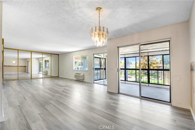 2384 Via Mariposa W Unit 3G, Laguna Woods, CA 92637 - empty room featuring a textured ceiling, a chandelier, a wall mounted AC, wood finished floors, and plenty of natural light