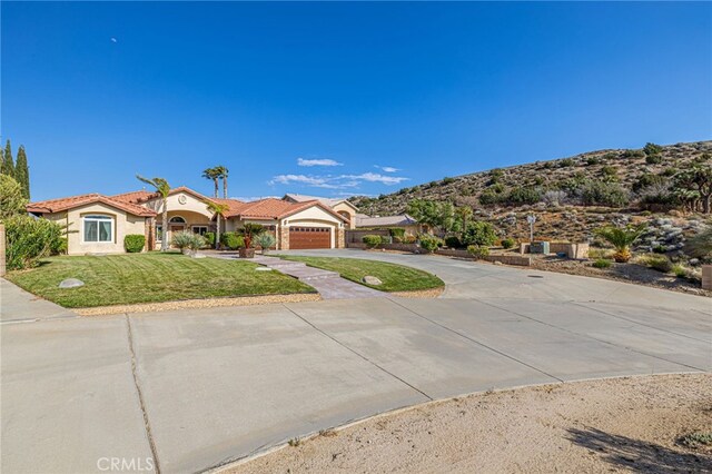 mediterranean / spanish-style home featuring curved driveway, a front yard, stucco siding, an attached garage, and a mountain view