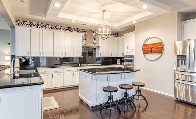 kitchen featuring appliances with stainless steel finishes, a sink, wall chimney exhaust hood, dark countertops, and baseboards