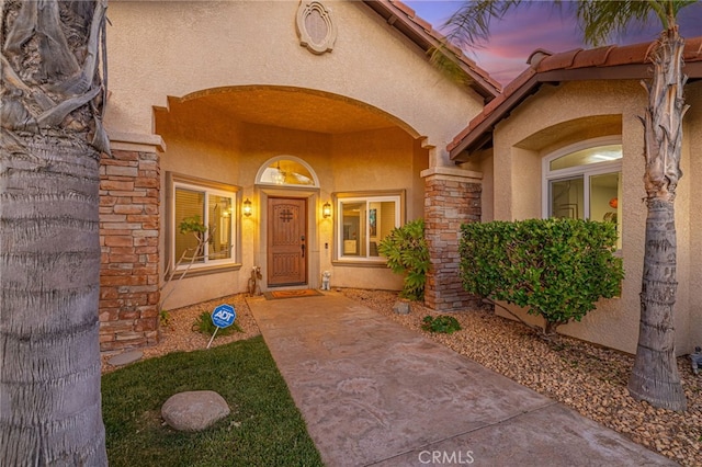exterior entry at dusk featuring stucco siding and stone siding