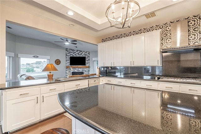 kitchen featuring a sink, a peninsula, a ceiling fan, tasteful backsplash, and white cabinets