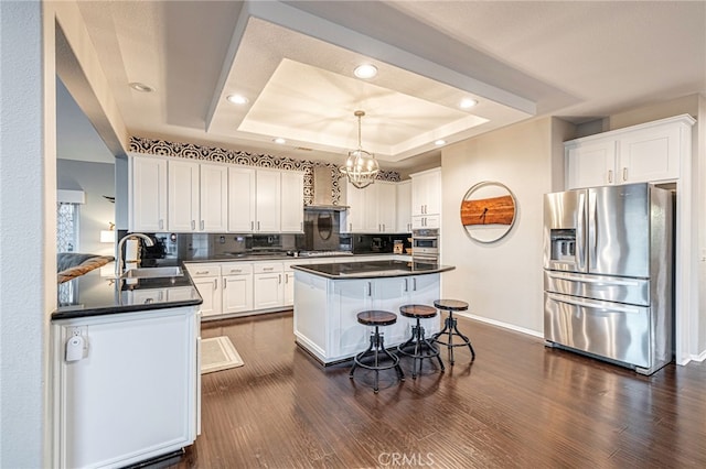 kitchen with stainless steel fridge with ice dispenser, a tray ceiling, dark countertops, white cabinetry, and recessed lighting