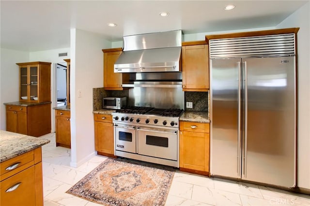 18041 Acre St, Northridge, CA 91325 - kitchen featuring premium appliances, wall chimney range hood, light marble finish flooring, brown cabinetry, and light stone countertops