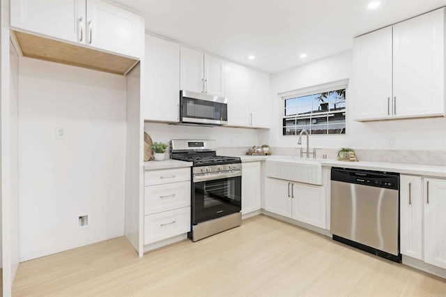 kitchen featuring stainless steel appliances, a sink, white cabinetry, light countertops, and recessed lighting
