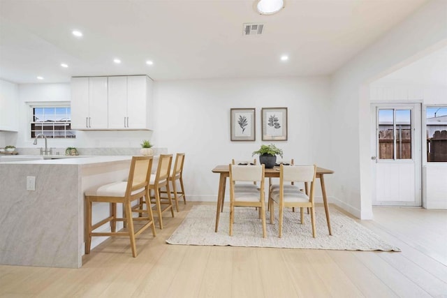 kitchen featuring white cabinets, light wood-type flooring, a breakfast bar area, recessed lighting, and light countertops