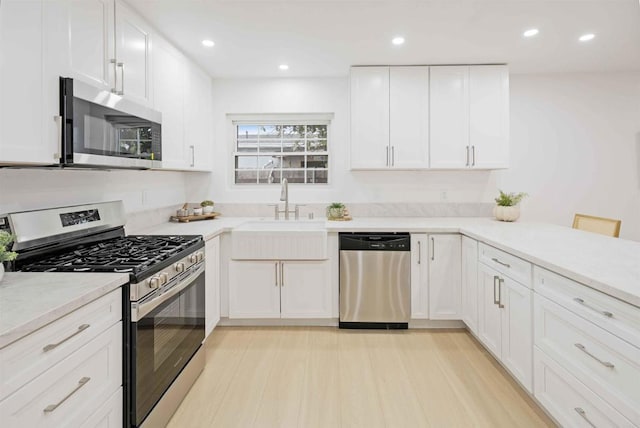 kitchen featuring appliances with stainless steel finishes, a sink, white cabinets, light countertops, and light wood-style floors