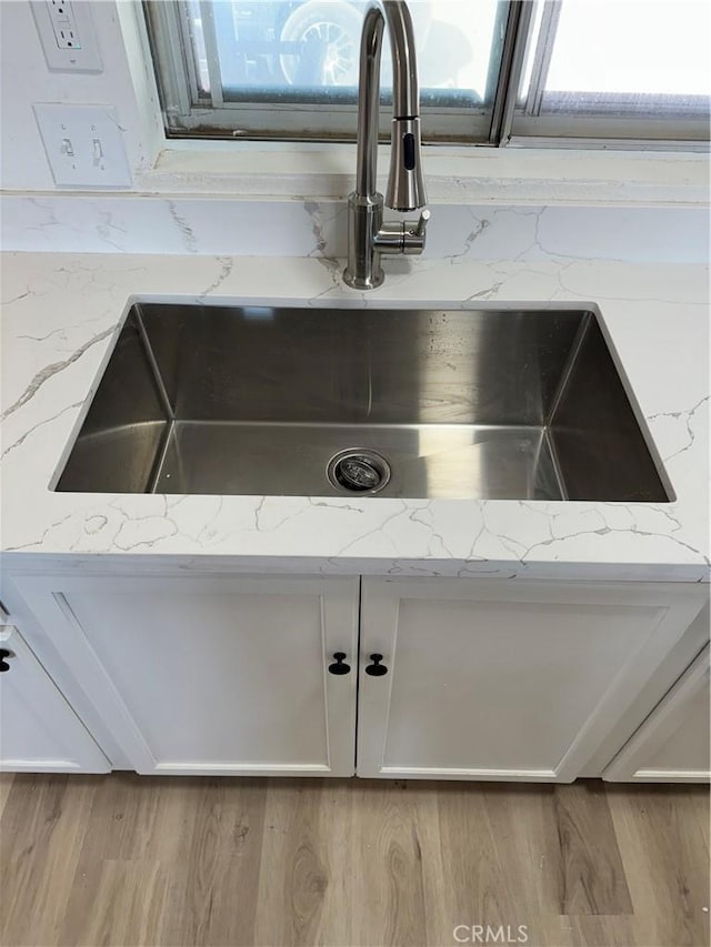kitchen view of a sink, white cabinetry, and light stone countertops
