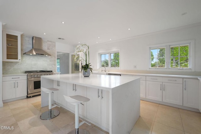 kitchen featuring wall chimney range hood, appliances with stainless steel finishes, decorative backsplash, a kitchen island, and light countertops