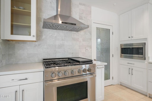 kitchen featuring stainless steel appliances, wall chimney exhaust hood, light countertops, white cabinets, and glass insert cabinets