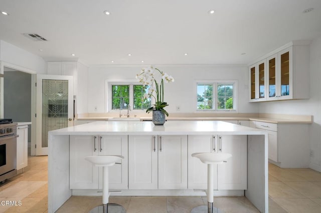 kitchen featuring stainless steel range with gas cooktop, healthy amount of natural light, glass insert cabinets, white cabinets, and recessed lighting