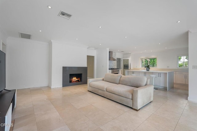 living area with crown molding, a warm lit fireplace, recessed lighting, and light tile patterned floors