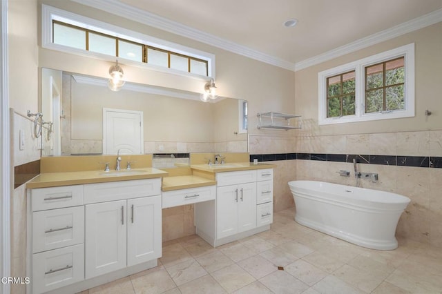 full bath with double vanity, crown molding, a soaking tub, tile walls, and a wainscoted wall