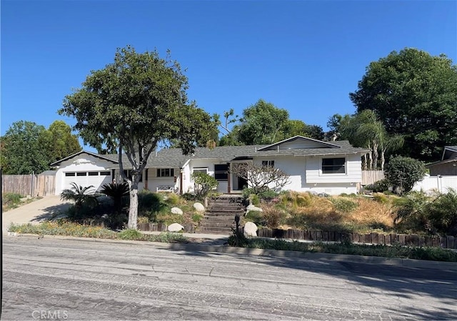 ranch-style home with driveway, fence, an attached garage, and stucco siding